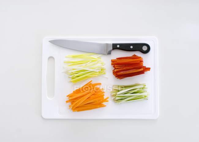 Legumes Julienne em uma tábua de corte com uma faca sobre a superfície branca — Fotografia de Stock