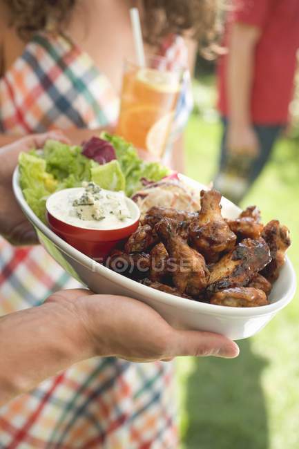 Vista cortada de mãos segurando asas de frango com salada — Fotografia de Stock