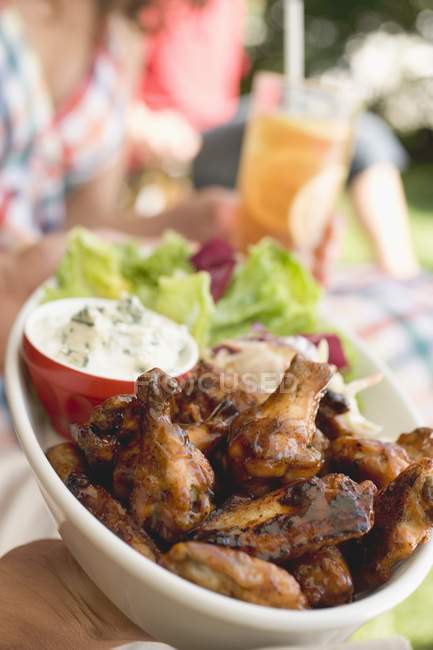Обрезанный вид рук с куриными крылышками и салатом — стоковое фото