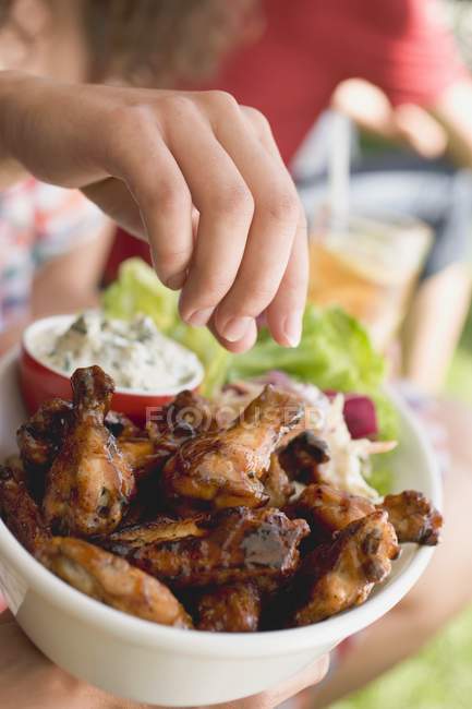 Primo piano vista della mano che raggiunge per le ali di pollo alla griglia — Foto stock