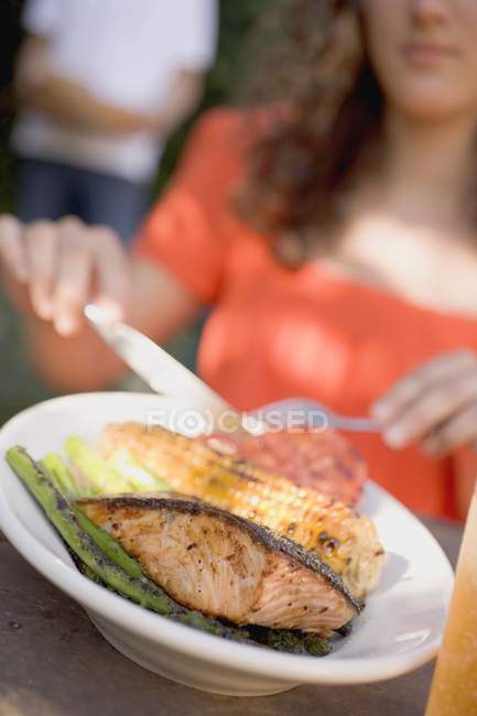 Женщина ест рыбу-гриль с кукурузой — стоковое фото