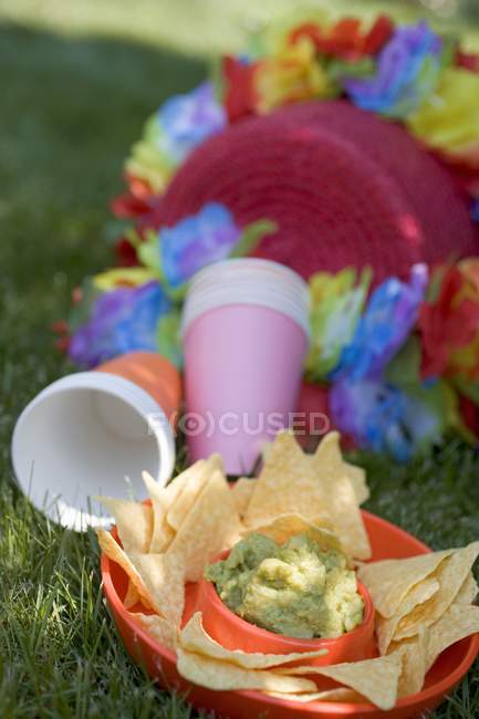 Guacamole con tortilla chips, bicchieri di carta e ghirlande colorate — Foto stock
