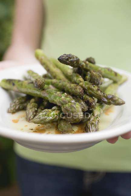 Hand holding plate of grilled asparagus — Stock Photo