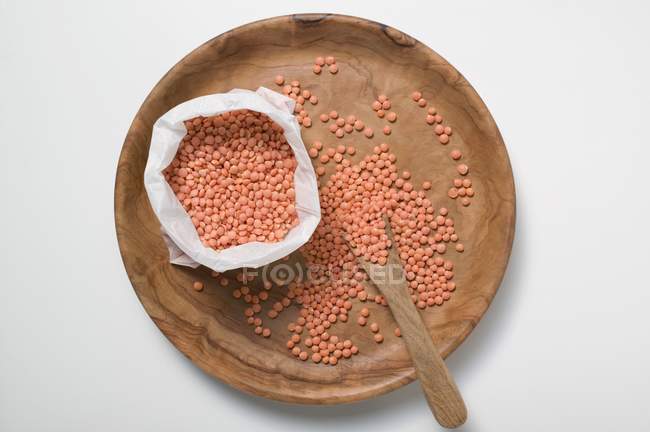 Top view of red lentils on wooden plate and in bag — Stock Photo