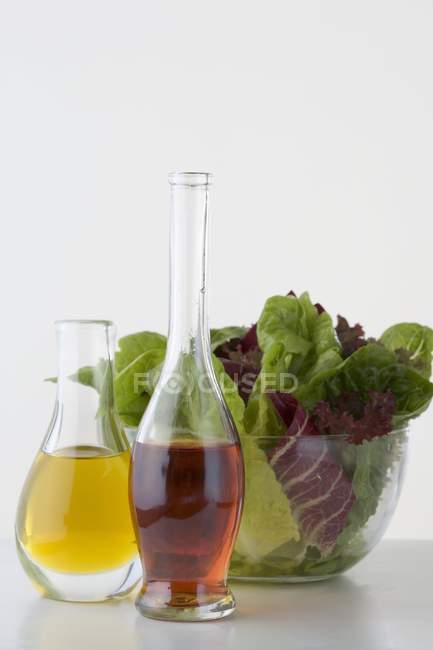 Closeup view of oil and vinegar in carafes in front of salad bowl — Stock Photo