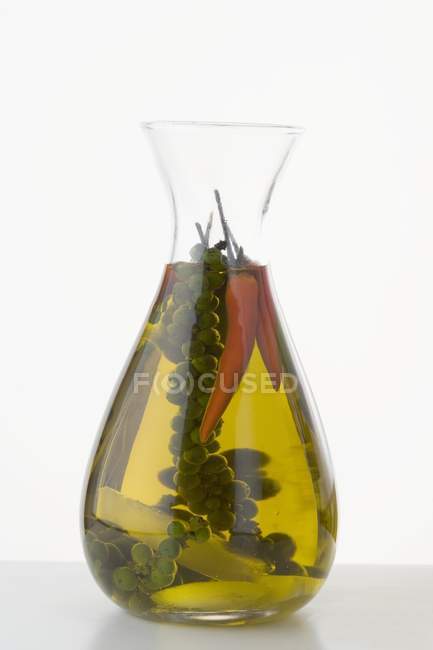 Aceite de chile con granos de pimienta verde en una jarra sobre fondo blanco - foto de stock