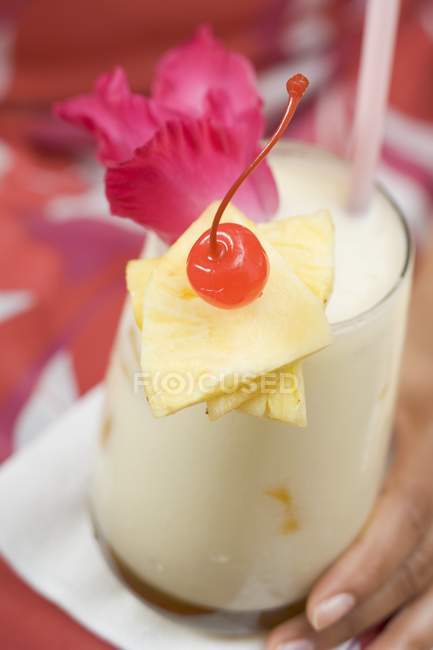 Primo piano vista ritagliata della mano femminile che tiene Pina Colada con fiore, fette di ananas e ciliegia — Foto stock