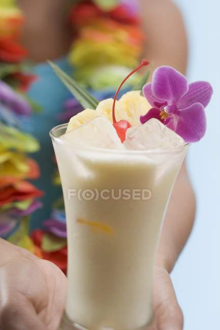 Vista ravvicinata della donna che tiene il bicchiere di Pina Colada con cubetti di ghiaccio, fiori e frutta — Foto stock