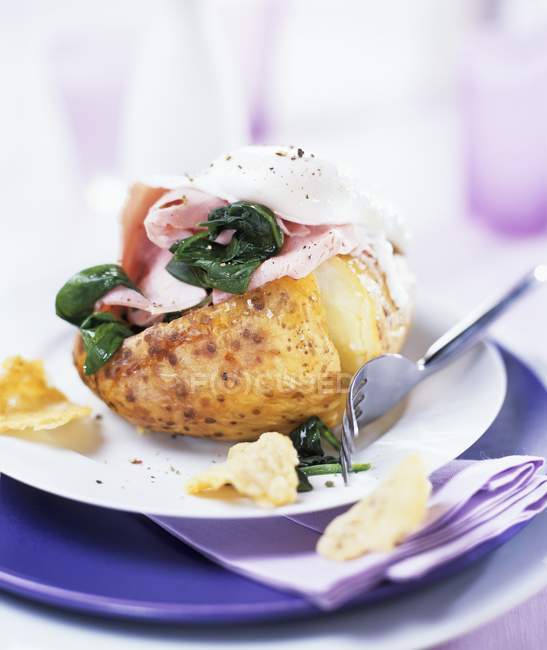 Batata assada com presunto, espinafre e ovo escalfado na placa branca com garfo — Fotografia de Stock