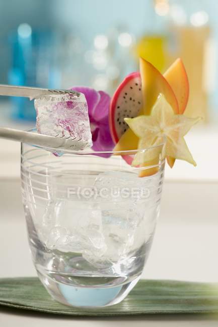Vista de cerca de poner cubo de hielo a copa de cóctel con rebanadas de fruta - foto de stock