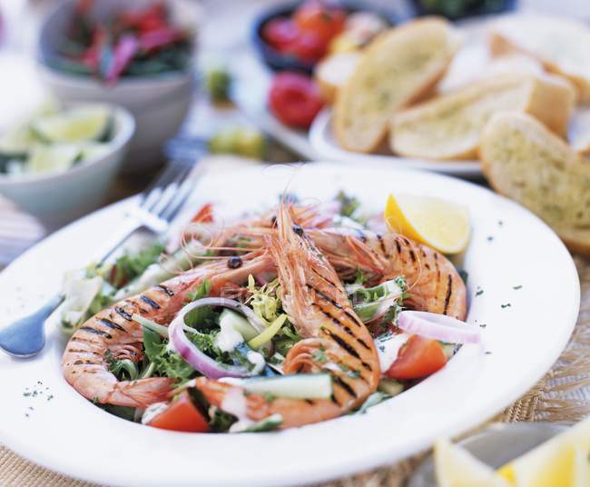 Closeup view of grilled prawns on vegetable salad with herb baguette — Stock Photo