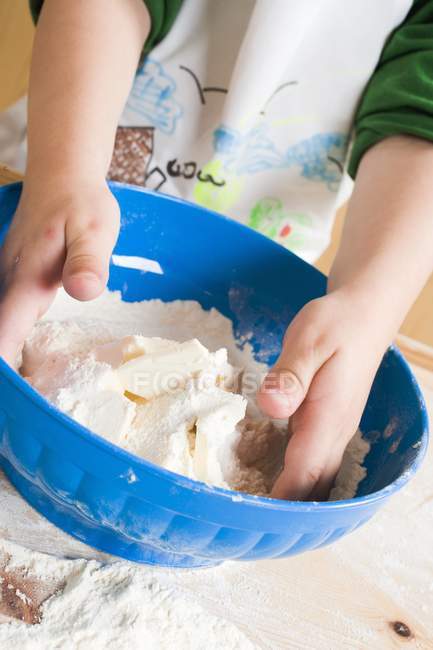 Vue rapprochée de l'enfant mélangeant farine et beurre dans un bol — Photo de stock