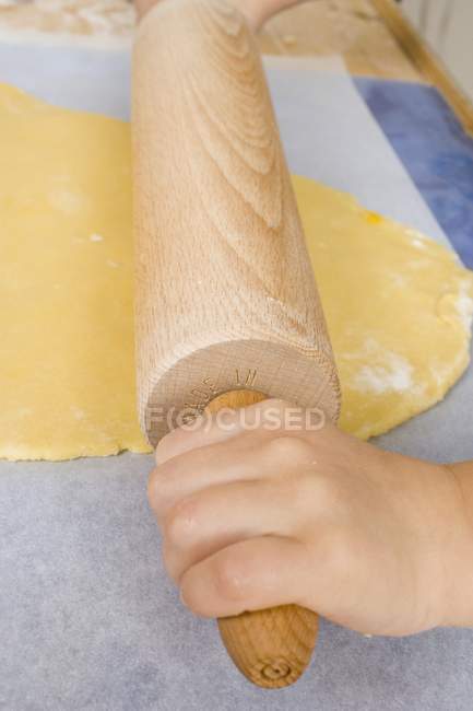 Vue rapprochée des mains de l'enfant déroulant la pâte — Photo de stock