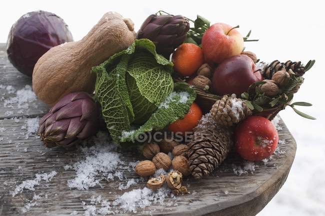 Вид крупным планом неподвижных яблок с овощами, орехами и шишками на деревянном столе — стоковое фото