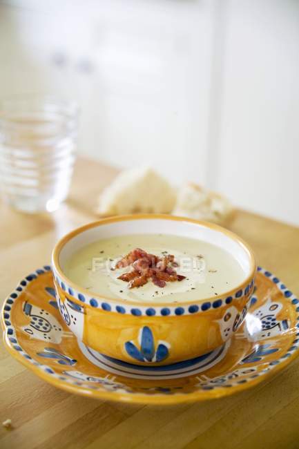 Fennel soup with bacon in colored bowl over plate on table — Stock Photo