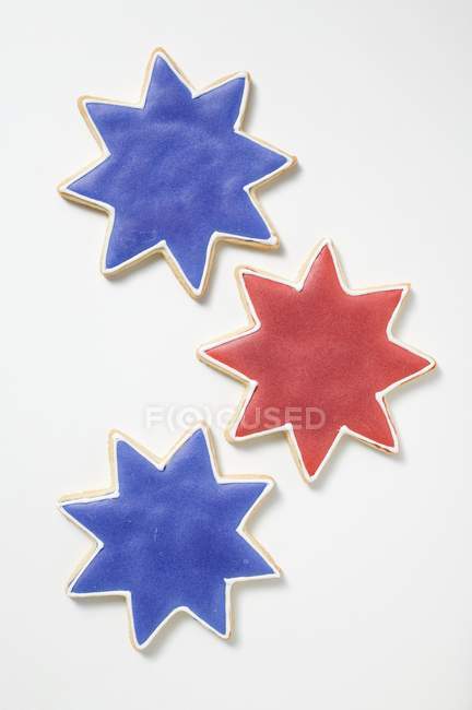 Vista de cerca de tres galletas en forma de estrella con glaseado rojo y azul - foto de stock