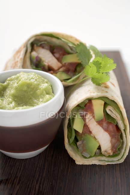 Closeup view of two chicken and avocado wraps with guacamole in small bowl — Stock Photo