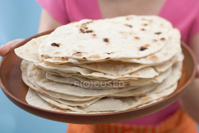 Vista de cerca de la mujer sosteniendo tortillas recién horneadas en la bandeja - foto de stock