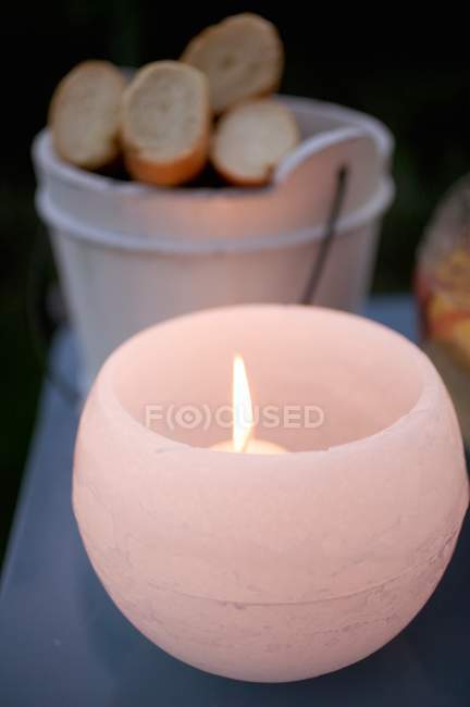 Nahaufnahme einer brennenden Kerze im Windlicht auf einem Gartentisch mit Baguette im Hintergrund — Stockfoto