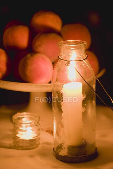 Closeup view of lit windlights and stand of peaches — Stock Photo