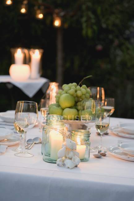 Bowl of fruit and windlights on table laid in garden — Stock Photo