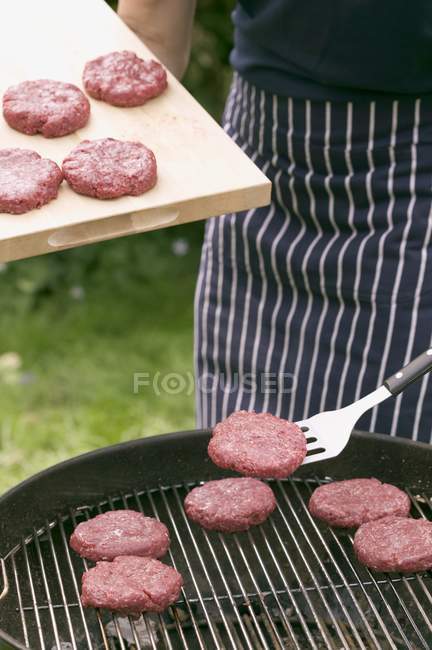 Uomo che mette hamburger crudi sulla griglia — Foto stock