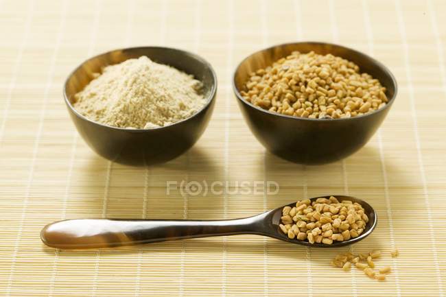Primo piano vista di semi di fieno greco non macinati e macinati in ciotole e su cucchiaio — Foto stock