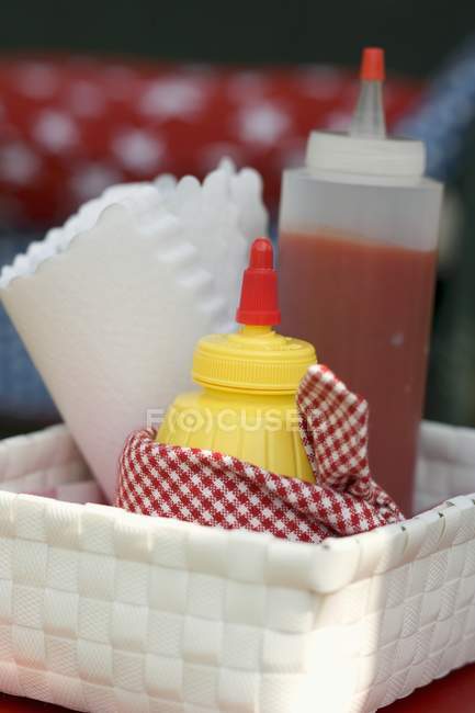 Vista de cerca de botellas de ketchup, mostaza y servilletas de papel en la cesta - foto de stock