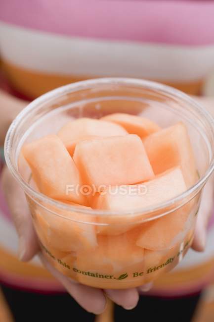 Woman holding plastic tub of melon — Stock Photo