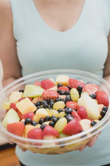 Cropped view of woman holding fruit salad in plastic bowl — Stock Photo