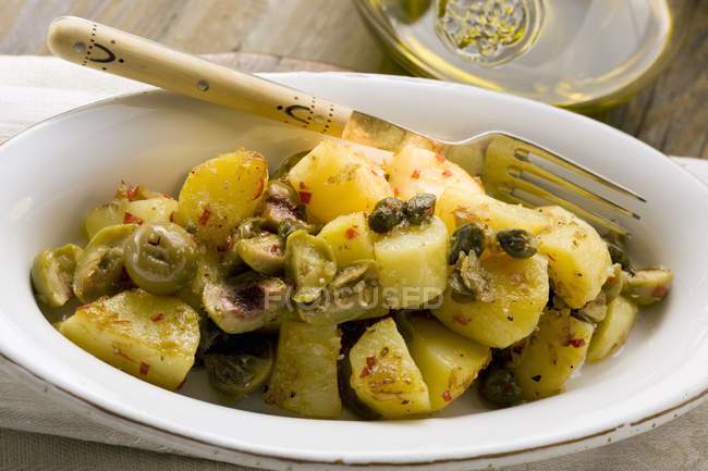 Spicy fried potatoes with olives and capers in serving dish — Stock Photo
