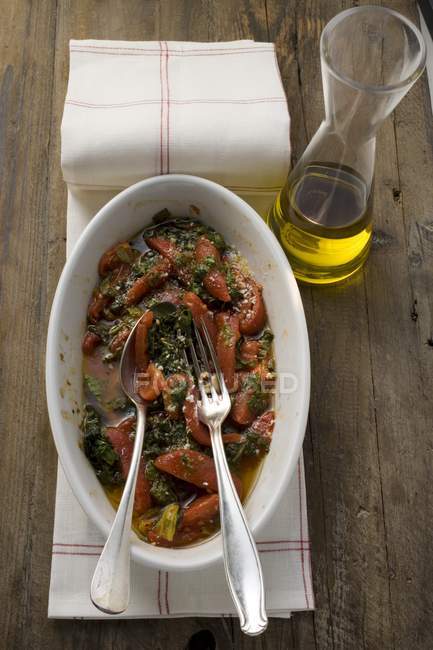 Tomates y col de col rizada, aceite de oliva en plato blanco sobre toalla sobre superficie de madera - foto de stock