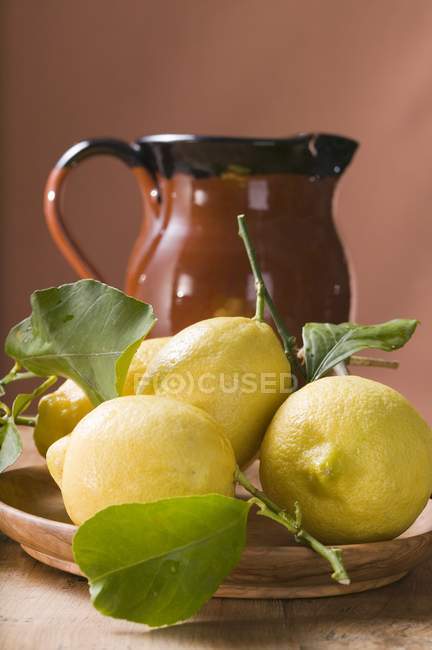 Limões frescos com folhas na placa — Fotografia de Stock