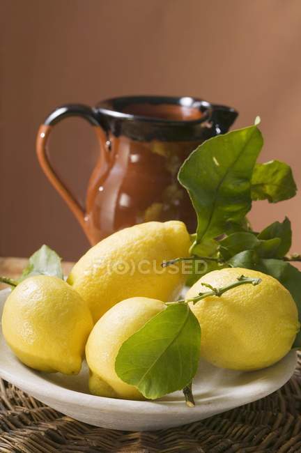 Limões frescos com folhas na placa — Fotografia de Stock