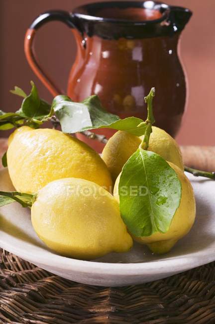 Limoni freschi con foglie sul piatto — Foto stock