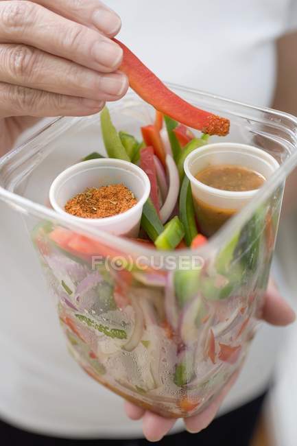 Woman holding plastic container of vegetables, seasonings dip, midsection — Stock Photo