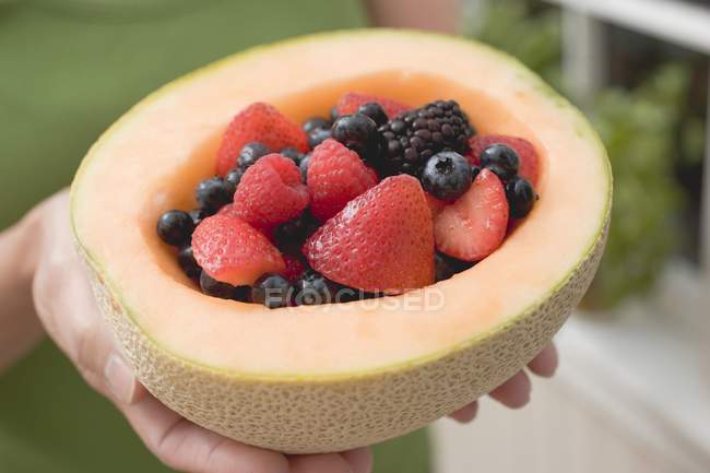 Woman holding fresh berries in melon — Stock Photo