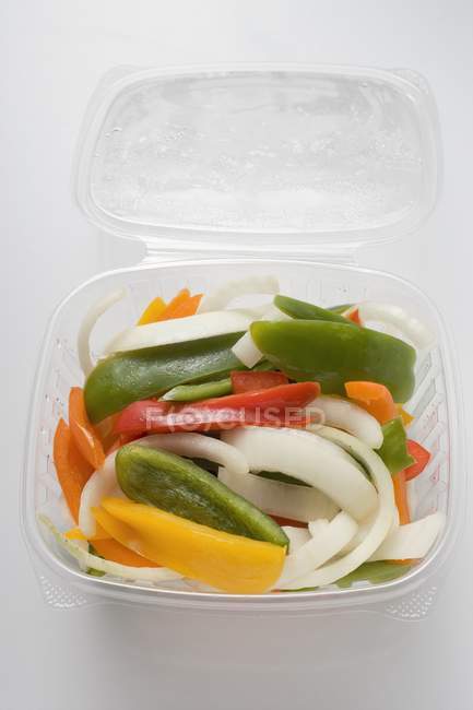 Legumes fatiados em recipiente plástico aberto na superfície branca — Fotografia de Stock