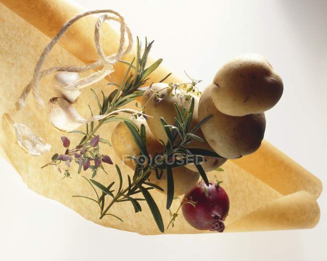 Potatoes with herbs, onion and garlic on baking parchment on white background — Stock Photo
