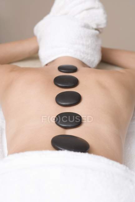 Lying woman having LaStone therapy with row of black stones on back — Stock Photo