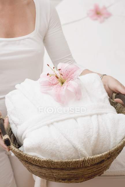 Vista cortada da mulher segurando roupão de banho branco e orquídea em cesta — Fotografia de Stock