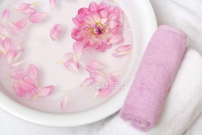 Vue du dessus des pétales de fleurs roses dans un bol d'eau avec des serviettes à côté — Photo de stock