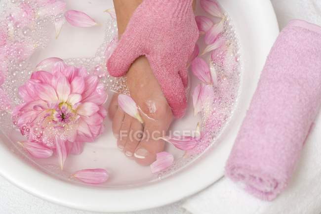 Повышенный вид на мытье женской ноги в успокаивающей ванне с лепестками цветов — стоковое фото