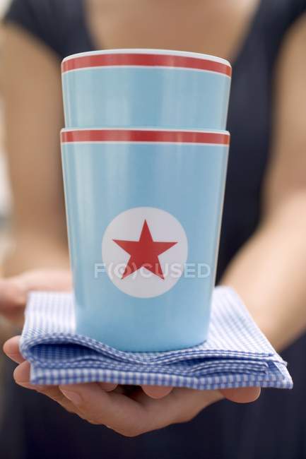 Вид крупным планом женщины, держащей две бумажные чашки со звездой на клетчатой ткани — стоковое фото