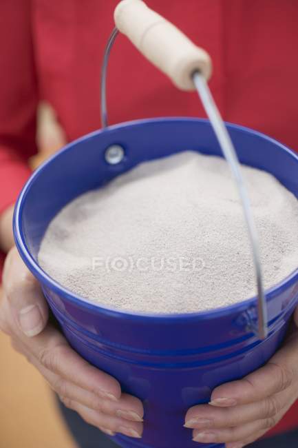 Woman holding blue bucket of sand — Stock Photo