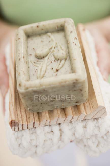 Женщина держит оливковое мыло на деревянном блюде и белом полотенце — стоковое фото