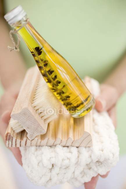 Woman holding bottle of body oil, soap dish, brush and towel — Stock Photo