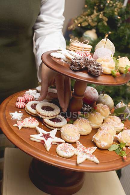 Cropped view of hand reaching for Christmas biscuit on tiered stand — Stock Photo