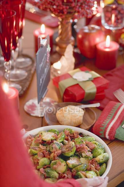 Woman serving Brussels sprouts with bacon in white dish — Stock Photo