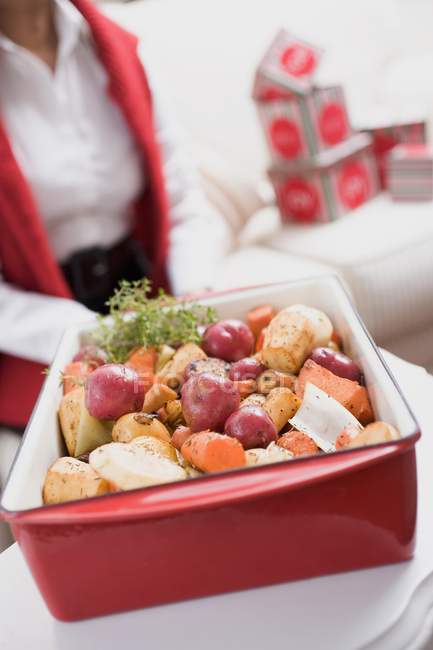 Roasted root vegetables in roasting dish, blurred woman in background — Stock Photo